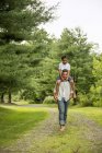 Menino pré-adolescente carregando irmão nos ombros enquanto caminha no caminho do campo . — Fotografia de Stock