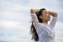 Mujer de pelo largo disfrutando de la brisa al aire libre contra el cielo nublado . - foto de stock
