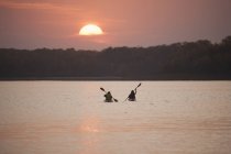 Dos kayakistas en barcos al atardecer en el tranquilo lago de Canadá . - foto de stock