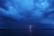 Удар молнии отражается в воде озера под темным бурным драматическим небом . — стоковое фото