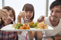 Grupo de alegres amigos japoneses compartiendo comida . - foto de stock