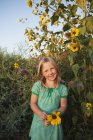 Vorpubertierendes Mädchen steht im Garten und hält Sonnenblumen in der Hand. — Stockfoto