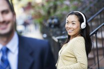 Mulher usando fones de ouvido de música e homem em terno de negócios andando em primeiro plano . — Fotografia de Stock
