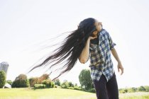 Junger Mann mit langen dunklen Haaren schüttelt den Kopf und tanzt an der frischen Luft. — Stockfoto