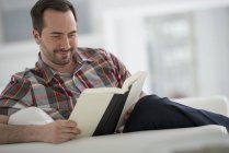 Mittlerer erwachsener Mann sitzt und liest Buch im hellen weißen Raum. — Stockfoto