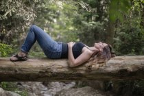 Жінка лежить на спині на падаючому стовбурі дерева в лісі . — стокове фото