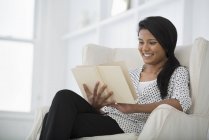 Giovane donna seduta sul divano bianco e libro di lettura . — Foto stock