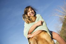 Pre-adolescent girl wrapped in beach towel playing with golden retriever dog. — Stock Photo