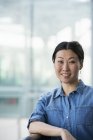 Asian woman in denim shirt sitting in front of modern building and smiling. — Stock Photo