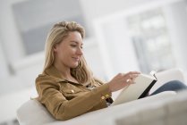 Blonde woman sitting and reading book in bright white room. — Stock Photo