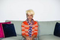 Смешанная расовая женщина с светлыми волосами сидит на диване и улыбается . — стоковое фото