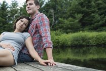 Молодая пара отдыхает на деревянной пристани с видом на горное озеро . — стоковое фото
