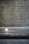 Lit candle on marble bench against brick wall. — Stock Photo