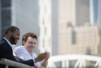 Two businessmen looking at smartphone while leaning on railing in downtown. — Stock Photo