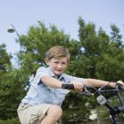 Elementary age boy riding bicycle and looking in camera in countryside. — Stock Photo