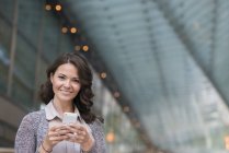 Giovane donna d'affari in cardigan grigio con smartphone e sorridente . — Foto stock