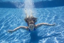 Pré-adolescente avec ventilateur cheveux longs nageant sous l'eau dans la piscine . — Photo de stock