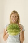 Vue de face de la femme blonde tenant une grande pastèque verte . — Photo de stock