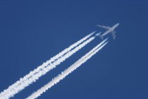Avião a jato em voo com trilhas no céu azul . — Fotografia de Stock