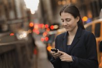 Geschäftsfrau checkt in der Abenddämmerung ihr Handy auf dem Bürgersteig der Stadt. — Stockfoto