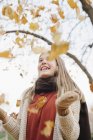 Веселая девочка-подросток бросает осенние листья в воздух в парке . — стоковое фото