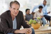 Mature man with wine sitting away from group of people at indoor party in background. — Stock Photo