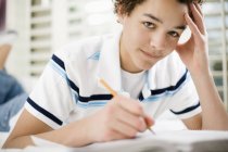 Pre-adolescent boy lying on front on bed and writing in school book. — Stock Photo