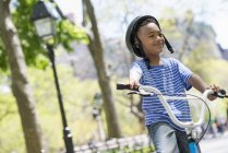 Menino de idade elementar andar de bicicleta e se divertir no parque ensolarado . — Fotografia de Stock