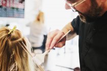 Homme coiffeur utilisant un pinceau pour teindre les cheveux blonds féminins . — Photo de stock