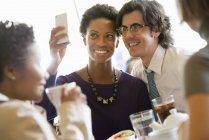 Hombre y mujer posando para selfie en la mesa del restaurante con amigos . - foto de stock