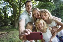 Сім'я з трьома дітьми, які беруть селфі на смартфон у парку . — стокове фото