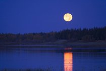 Lua cheia no céu noturno refletindo na água do lago no Canadá — Fotografia de Stock