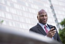 Low angle view of mid adult businessman using smartphone in city. — Stock Photo