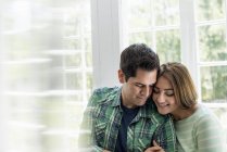 Young couple embracing indoors by window. — Stock Photo