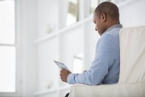 Seitenansicht eines Mannes, der im Sessel sitzt und digitales Tablet nutzt. — Stockfoto