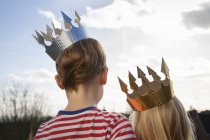Two children in fancy crowns standing outdoors, rear view. — Stock Photo