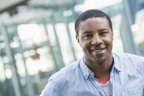 African american man in blue shirt standing in front modern building and smiling. — Stock Photo