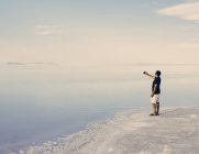 Man standing at edge of flooded Bonneville Salt Flats at dusk and taking picture with smartphone near Wendover, Utah, USA. — Stock Photo