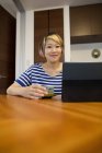 Femme japonaise assise à table avec ordinateur portable et thé vert et regardant à la caméra . — Photo de stock