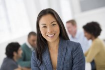 Cheerful businesswoman standing in meeting room with colleagues in background. — Stock Photo