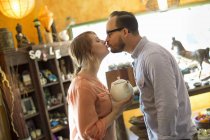 Hombre y mujer besando y sosteniendo la tetera en la tienda de antigüedades . - foto de stock