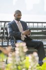 Empresário sentado no banco da cidade e verificando smartphone . — Fotografia de Stock