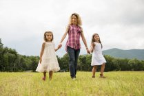 Mother walking hand in hand with daughters in rural field. — Stock Photo