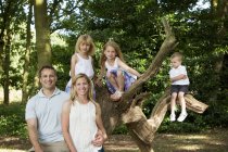 Сім'я з трьома дітьми, які позують разом на дереві в парку . — стокове фото