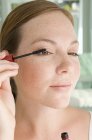 Young woman applying mascara to eyelashes, portrait. — Stock Photo