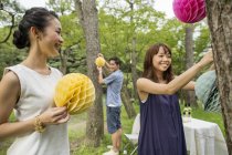 Group of people hanging paper lanterns on trees in woodland. — Stock Photo