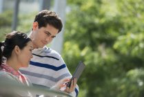Man and woman sharing digital tablet in city park. — Stock Photo