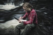 Mann sitzt am schnell fließenden Strom und nutzt digitales Tablet. — Stockfoto