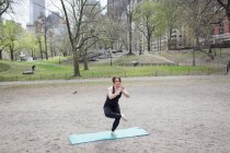 Mulher fazendo ioga em uma perna no tapete de ginástica no Central Park
. — Fotografia de Stock