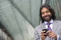 Мужчина в деловом костюме с бородой и вьющимися волосами с помощью смартфона . — стоковое фото